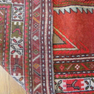 A low-pile rug with red, green, and cream geometric patterns is folded over on a wood floor.