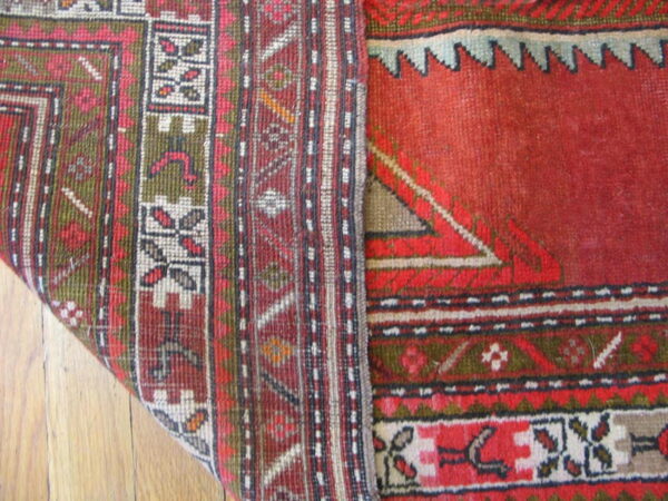 A low-pile rug with red, green, and cream geometric patterns is folded over on a wood floor.