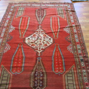 Low-pile red geometric rug with cream, blue, and brown accents displayed on hardwood planks.