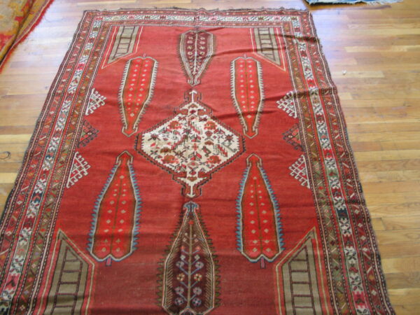 Low-pile red geometric rug with cream, blue, and brown accents displayed on hardwood planks.