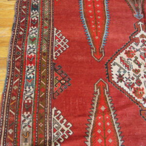 Geometric red rug features complex borders and stylized white, red, and blue diamond motifs on wood flooring.