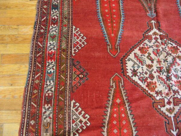 Geometric red rug features complex borders and stylized white, red, and blue diamond motifs on wood flooring.