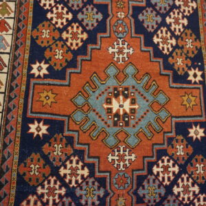 Geometric rug featuring a large stepped medallion in burnt orange, teal, and navy blue on wood floors.