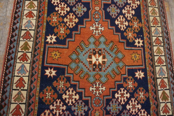 Geometric rug featuring a large stepped medallion in burnt orange, teal, and navy blue on wood floors.