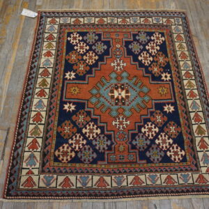Navy and terracotta geometric rug with complex patterns placed on a worn, gray wood floor.