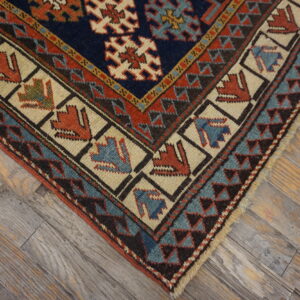Geometric rug corner in navy, rust, and teal with stylized figures rests on distressed gray wood flooring.