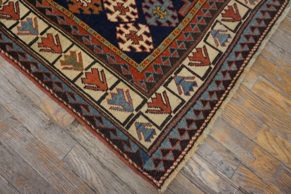 Geometric rug corner in navy, rust, and teal with stylized figures rests on distressed gray wood flooring.