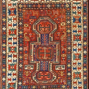 A tightly patterned red rug features complex geometric medallions, stylized animals, and wide borders in navy, cream, and teal.
