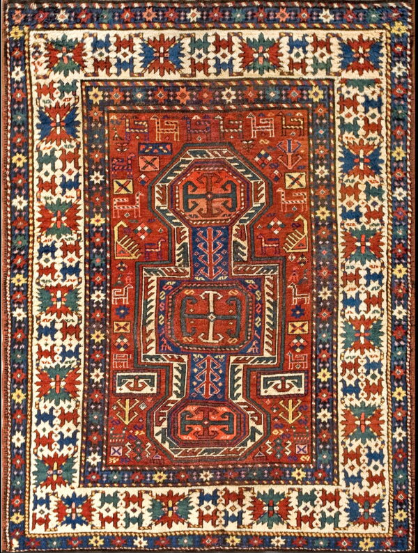 A tightly patterned red rug features complex geometric medallions, stylized animals, and wide borders in navy, cream, and teal.