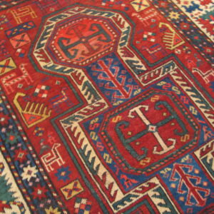Red tribal rug featuring complex geometric borders and stylized animal shapes in blue, cream, and teal.