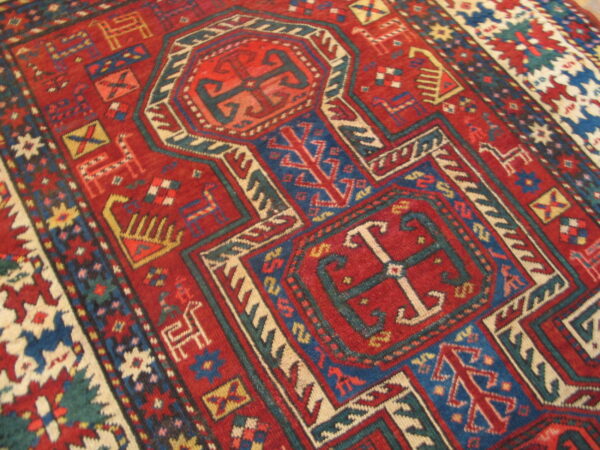Red tribal rug featuring complex geometric borders and stylized animal shapes in blue, cream, and teal.