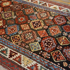 Geometric rug with a dark field, colorful star medallions, and stepped borders lying on wood planks.