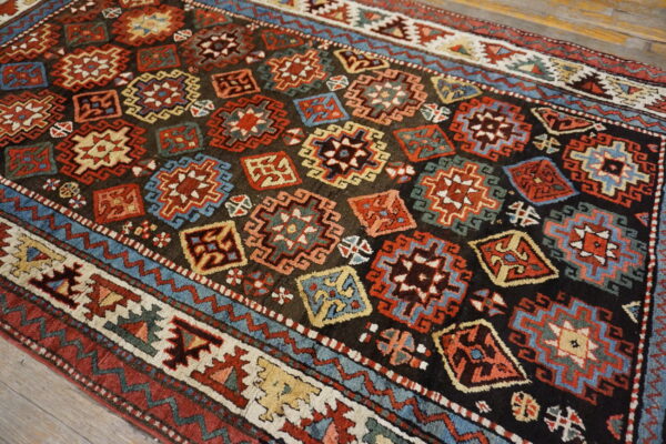 Geometric rug with a dark field, colorful star medallions, and stepped borders lying on wood planks.