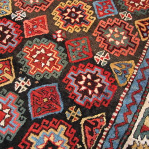 Geometric rug detail showing repeating red, blue, and gold stepped motifs on a dark field and patterned border.