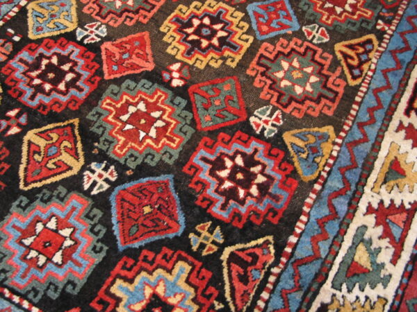Geometric rug detail showing repeating red, blue, and gold stepped motifs on a dark field and patterned border.