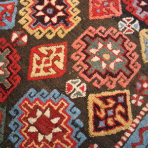 Close-up showing multicolored geometric motifs in red, blue, and cream on a dark brown textured pile.