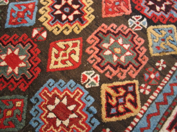 Close-up showing multicolored geometric motifs in red, blue, and cream on a dark brown textured pile.