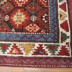 High-pile tribal rug corner in rich red and blue features stepped geometric motifs on a wood floor.