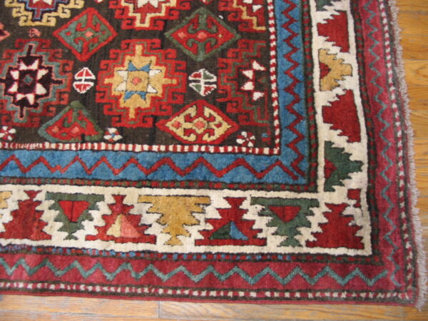 High-pile tribal rug corner in rich red and blue features stepped geometric motifs on a wood floor.