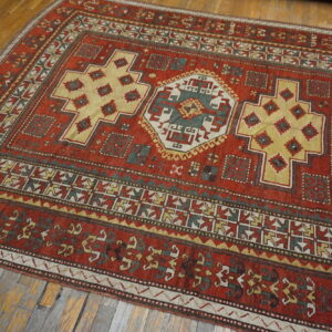 A richly patterned rust red rug featuring yellow and teal medallions rests on worn wood planks.