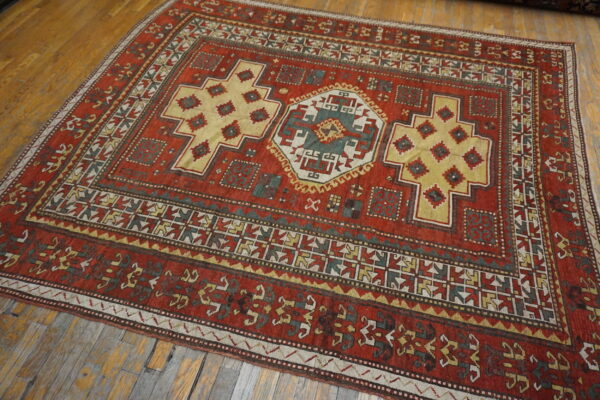 A richly patterned rust red rug featuring yellow and teal medallions rests on worn wood planks.