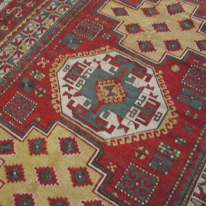 Geometric red rug featuring a central medallion and stepped borders in gold, teal, and cream colors.
