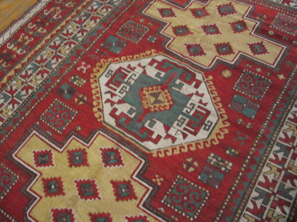 Geometric red rug featuring a central medallion and stepped borders in gold, teal, and cream colors.