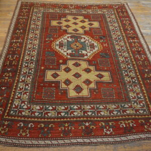 A rust red rug with geometric yellow, green, and cream patterns rests on a distressed wood plank floor.