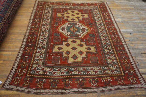 A rust red rug with geometric yellow, green, and cream patterns rests on a distressed wood plank floor.