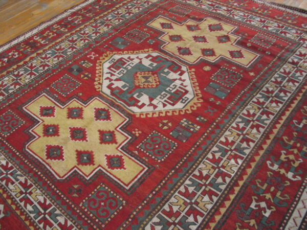 Red geometric rug with stepped gold and teal medallions rests on light wooden plank flooring.