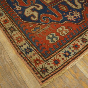 Geometric rug corner showing red and blue central field with tan borders on distressed wood planks.