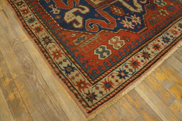 Geometric rug corner showing red and blue central field with tan borders on distressed wood planks.