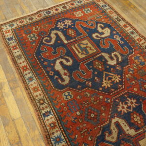 A low-pile rug with a geometric blue and red pattern and beige accents lies on distressed wood floors.