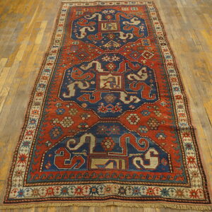 Rust-red and navy geometric patterned runner rug featuring stylized motifs rests on light wood plank flooring.