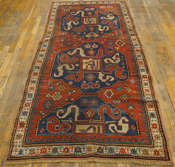 Rust-red and navy geometric patterned runner rug featuring stylized motifs rests on light wood plank flooring.