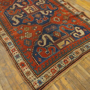 A deeply colored rug featuring red, blue, and tan geometric motifs rests on distressed wood flooring.