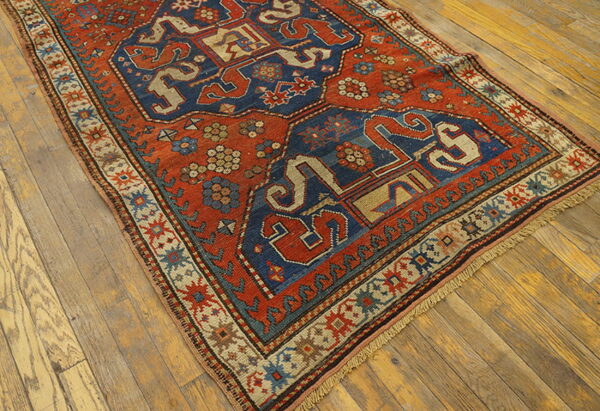 A deeply colored rug featuring red, blue, and tan geometric motifs rests on distressed wood flooring.