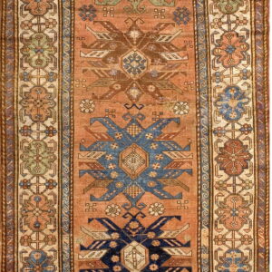 Geometric runner rug with an apricot field and repeating dark blue, brown, and green tribal designs.