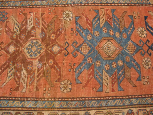 Geometric tribal rug detail featuring a rust field with contrasting blue and brown stylized star motifs and patterned borders.