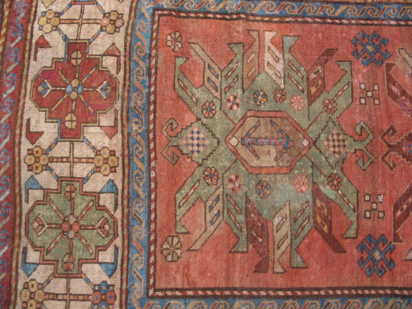 Detailed view of a low-pile geometric rug with rust field, sage motifs, and a cream-ground border.