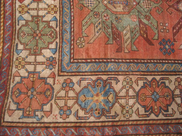 Detailed view of a low pile rug featuring rust, cream, blue, and green geometric motifs and borders.