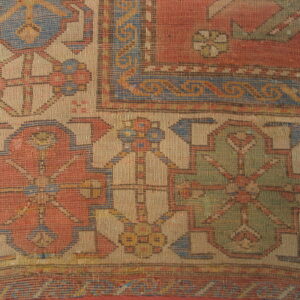 Geometric pattern detail of a tightly woven rug in terracotta, tan, blue, and olive green colors.