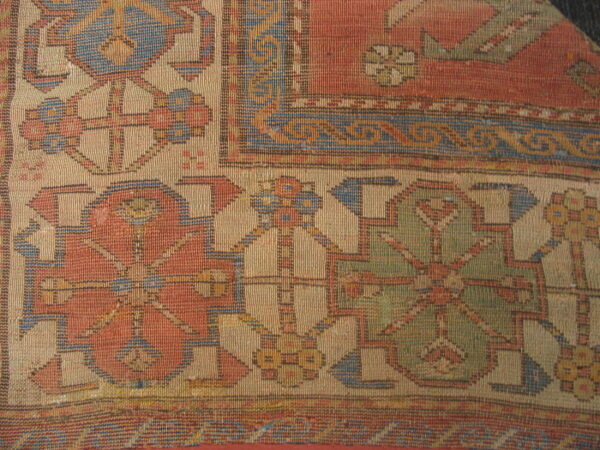 Geometric pattern detail of a tightly woven rug in terracotta, tan, blue, and olive green colors.