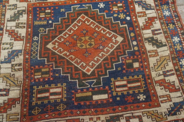 Stepped diamond medallion rug in rust, navy, cream, and brown, displaying dense tribal geometric patterns.