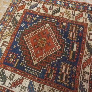 Traditional geometric rug with a red center diamond and navy blue field, lying on distressed wood floors.