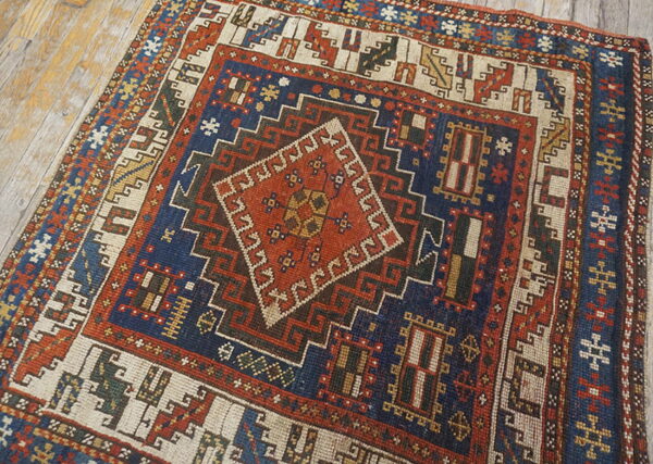 Traditional geometric rug with a red center diamond and navy blue field, lying on distressed wood floors.