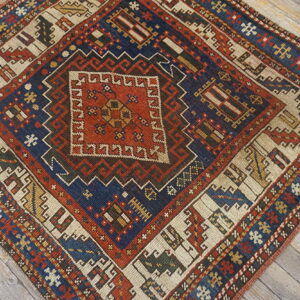 Geometric small rug displaying a complex central diamond pattern in navy, terracotta, and cream on gray wood.