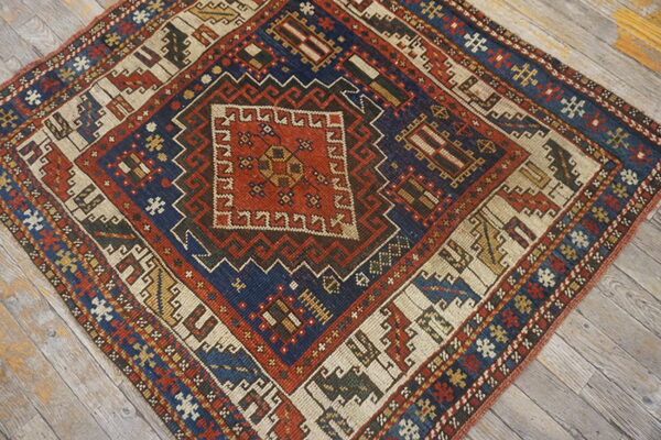 Geometric small rug displaying a complex central diamond pattern in navy, terracotta, and cream on gray wood.