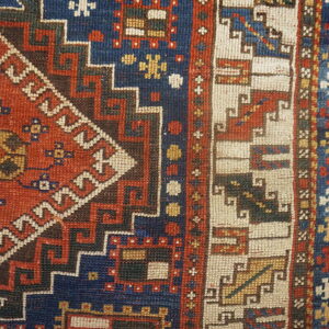 Close-up of a rug featuring geometric patterns in navy, rust, cream, and dark brown colors.