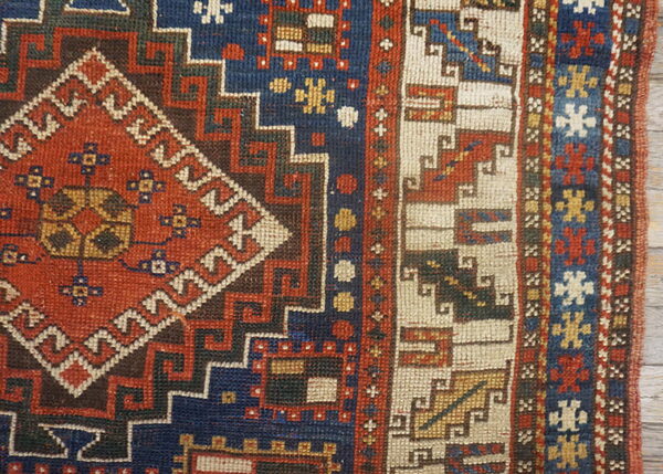 Close-up of a rug featuring geometric patterns in navy, rust, cream, and dark brown colors.